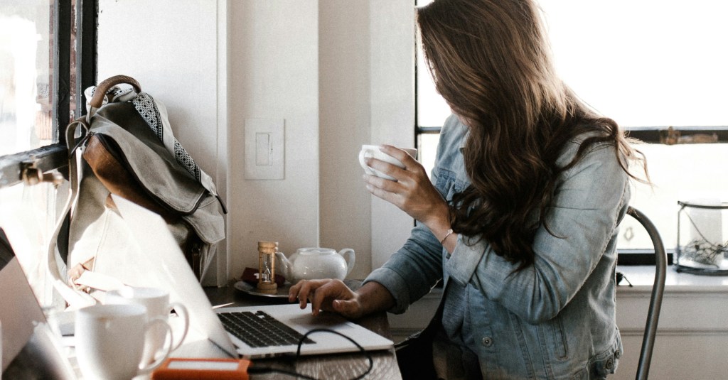 A woman sipping coffee while typing on a laptop computer