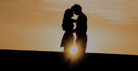 A silhouette of a man and a woman embracing with a sunset behind them.