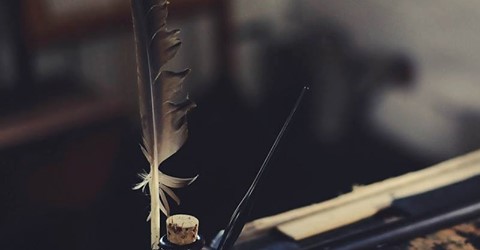 A desk with the image focus being on a feather quill